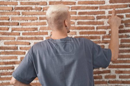 Photo for Young caucasian man standing over bricks wall posing backwards pointing ahead with finger hand - Royalty Free Image