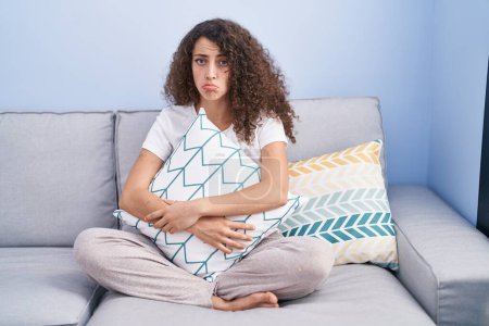 Photo for Hispanic woman with curly hair sitting on the sofa at home depressed and worry for distress, crying angry and afraid. sad expression. - Royalty Free Image