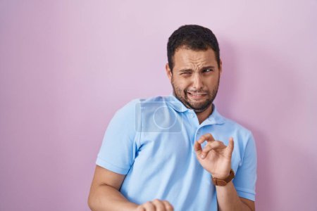Foto de Hombre hispano de pie sobre fondo rosa expresión disgustada, disgustado y temeroso haciendo cara disgusto porque reacción aversión. - Imagen libre de derechos
