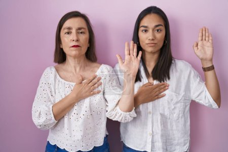 Téléchargez les photos : Mère et fille hispaniques jurant ensemble la main sur la poitrine et la paume ouverte, prêtant serment de fidélité - en image libre de droit