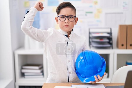Foto de Joven niño hispano sosteniendo el arquitecto hardhat en la oficina molesto y frustrado gritando con ira, gritando loco de ira y mano levantada - Imagen libre de derechos
