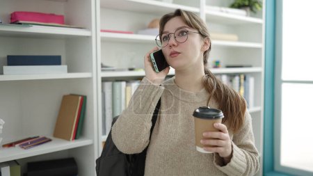 Téléchargez les photos : Young blonde woman student talking on smartphone drinking coffee at library university - en image libre de droit