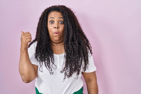 Photo for Plus size hispanic woman standing over pink background surprised pointing with hand finger to the side, open mouth amazed expression. - Royalty Free Image