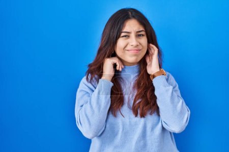 Photo for Hispanic young woman standing over blue background covering ears with fingers with annoyed expression for the noise of loud music. deaf concept. - Royalty Free Image