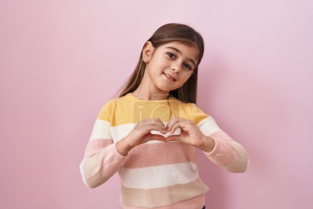 Photo for Little hispanic girl wearing sweater over pink background smiling in love doing heart symbol shape with hands. romantic concept. - Royalty Free Image