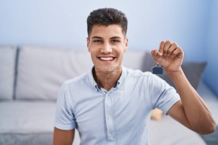 Foto de Joven hombre hispano sosteniendo las llaves de un nuevo hogar luciendo positivo y feliz de pie y sonriendo con una sonrisa confiada mostrando los dientes - Imagen libre de derechos