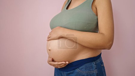 Foto de Mujer embarazada joven tocando el vientre sobre fondo rosa aislado - Imagen libre de derechos