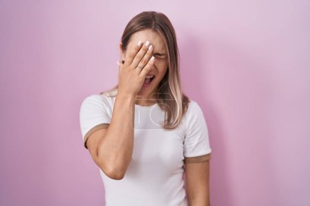 Photo for Blonde caucasian woman standing over pink background yawning tired covering half face, eye and mouth with hand. face hurts in pain. - Royalty Free Image