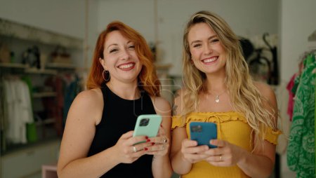 Photo for Two women smiling confident using smartphones at clothing store - Royalty Free Image