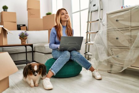 Foto de Joven mujer caucásica usando portátil sentado con el perro en el nuevo hogar - Imagen libre de derechos
