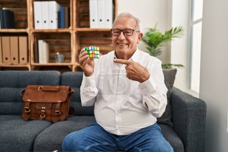 Photo for Senior therapist with grey hair playing colorful puzzle cube intelligence game smiling happy pointing with hand and finger - Royalty Free Image
