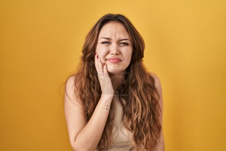 Téléchargez les photos : Young hispanic woman standing over yellow background touching mouth with hand with painful expression because of toothache or dental illness on teeth. dentist - en image libre de droit