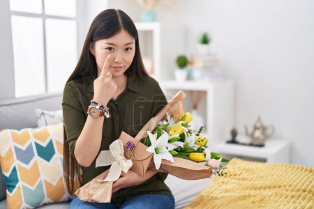 Photo for Chinese young woman holding bouquet of white flowers pointing to the eye watching you gesture, suspicious expression - Royalty Free Image