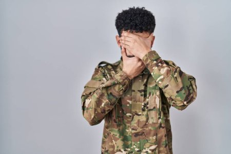 Téléchargez les photos : Homme arabe portant uniforme de camouflage de l'armée couvrant les yeux et la bouche avec les mains, surpris et choqué. cacher l'émotion - en image libre de droit