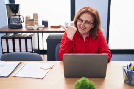 Photo for Senior woman with glasses working at the office with laptop pointing thumb up to the side smiling happy with open mouth - Royalty Free Image