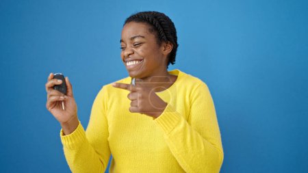Photo for African american woman smiling confident pointing to key of new car over isolated blue background - Royalty Free Image