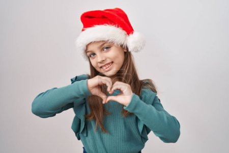 Foto de Niña caucásica con sombrero de navidad sonriendo en el amor haciendo forma de símbolo del corazón con las manos. concepto romántico. - Imagen libre de derechos