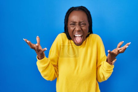 Photo for Beautiful black woman standing over blue background celebrating mad and crazy for success with arms raised and closed eyes screaming excited. winner concept - Royalty Free Image