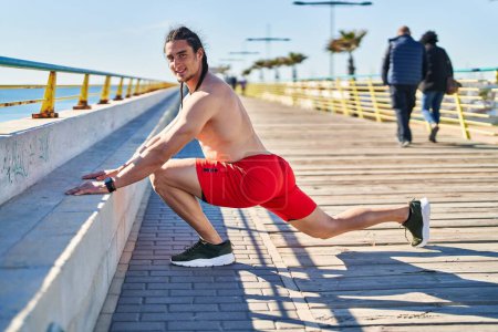 Téléchargez les photos : Jeune homme souriant confiant étirant les jambes au bord de la mer - en image libre de droit