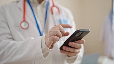 Téléchargez les photos : Jeune homme hispanique médecin en utilisant un smartphone à la clinique - en image libre de droit