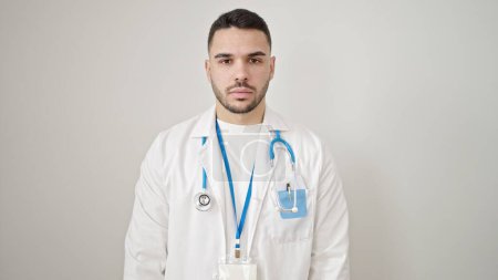 Foto de Joven médico hispano de pie con expresión seria sobre fondo blanco aislado - Imagen libre de derechos