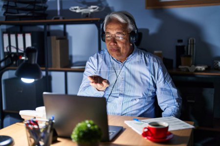 Photo for Hispanic senior man wearing call center agent headset at night looking at the camera blowing a kiss with hand on air being lovely and sexy. love expression. - Royalty Free Image