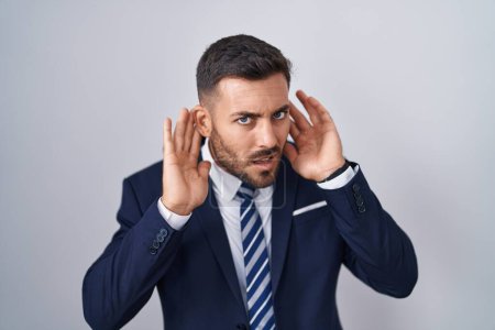 Téléchargez les photos : Un bel homme hispanique portant costume et cravate essayant d'entendre les deux mains sur le geste de l'oreille, curieux de commérages. problème auditif, sourd - en image libre de droit