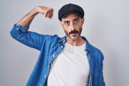 Foto de Hombre hispano con barba de pie sobre un fondo aislado persona fuerte que muestra el músculo del brazo, confiado y orgulloso de poder - Imagen libre de derechos