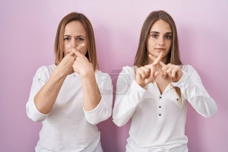 Téléchargez les photos : Mère d'âge moyen et jeune fille debout sur fond rose expression de rejet en croisant les doigts faisant signe négatif - en image libre de droit