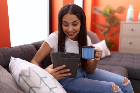 Téléchargez les photos : Young arab woman using touchpad drinking coffee sitting on sofa at home - en image libre de droit