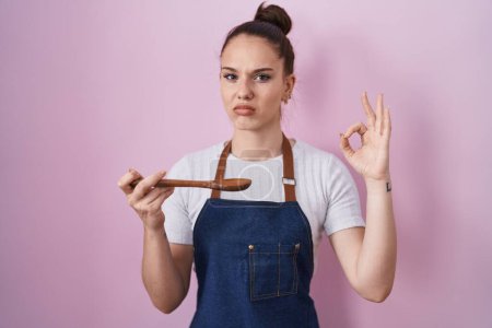 Photo for Young hispanic girl wearing professional cook apron holding wood spoon skeptic and nervous, frowning upset because of problem. negative person. - Royalty Free Image
