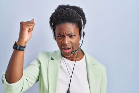 Téléchargez les photos : Femme afro-américaine portant casque agent du centre d'appel en colère et fou levant le poing frustré et furieux tout en criant avec colère. rage et concept agressif. - en image libre de droit