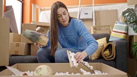 Photo for Young caucasian woman unpacking cardboard box at new home - Royalty Free Image