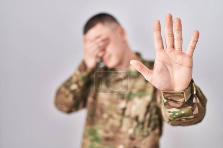Photo for Young man wearing camouflage army uniform covering eyes with hands and doing stop gesture with sad and fear expression. embarrassed and negative concept. - Royalty Free Image