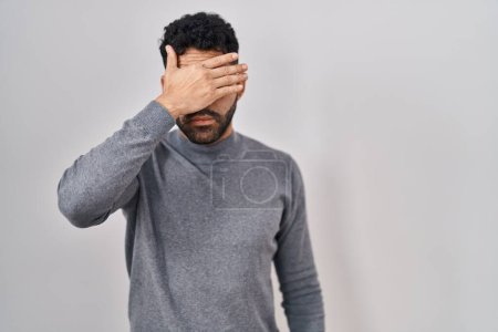 Photo for Hispanic man with beard standing over white background covering eyes with hand, looking serious and sad. sightless, hiding and rejection concept - Royalty Free Image