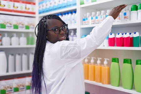 Foto de Farmacéutica afroamericana sostiene producto en estanterías en farmacia - Imagen libre de derechos
