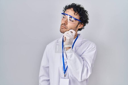 Téléchargez les photos : L'homme hispanique travaillant au laboratoire scientifique pense concentré sur le doute avec le doigt sur le menton et regardant vers le haut se demandant - en image libre de droit