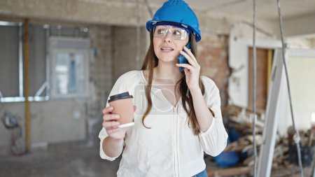 Téléchargez les photos : Jeune belle hispanique femme constructeur parler sur smartphone boire du café sur le site de construction - en image libre de droit