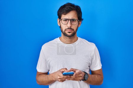Photo for Handsome latin man using smartphone typing message depressed and worry for distress, crying angry and afraid. sad expression. - Royalty Free Image