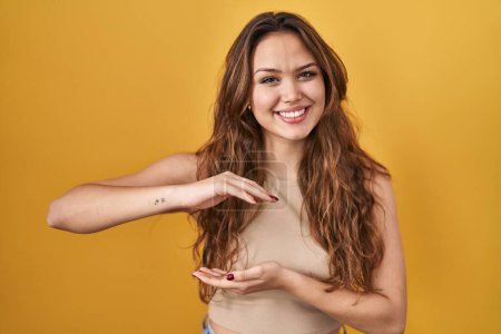 Téléchargez les photos : Young hispanic woman standing over yellow background gesturing with hands showing big and large size sign, measure symbol. smiling looking at the camera. measuring concept. - en image libre de droit