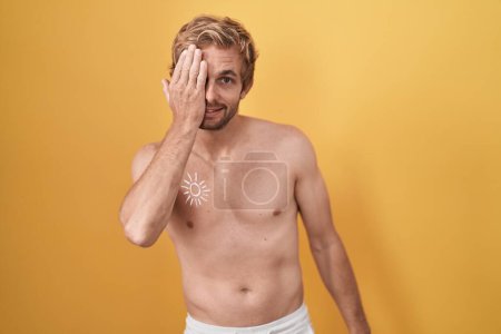 Téléchargez les photos : Homme caucasien debout torse nu portant un écran solaire couvrant un oeil avec la main, sourire confiant sur le visage et l'émotion surprise. - en image libre de droit