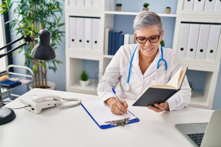 Photo for Middle age woman wearing doctor uniform writing on clipboard at clinic - Royalty Free Image