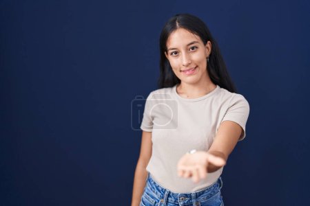 Téléchargez les photos : Jeune femme hispanique debout sur fond bleu souriant joyeuse offrant main de paume donnant assistance et acceptation. - en image libre de droit