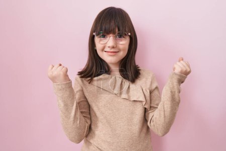 Téléchargez les photos : Petite fille hispanique portant des lunettes criant fier, célébrant la victoire et le succès très excité avec les bras levés - en image libre de droit