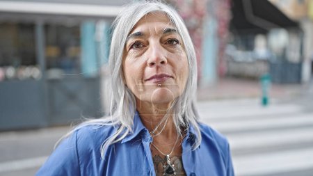 Foto de Mujer de pelo gris de mediana edad de pie con expresión seria en la calle - Imagen libre de derechos
