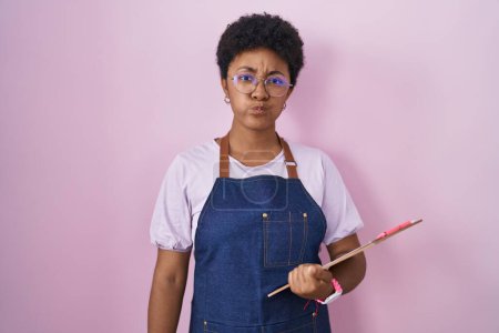 Photo for Young african american woman wearing professional waitress apron holding clipboard puffing cheeks with funny face. mouth inflated with air, crazy expression. - Royalty Free Image