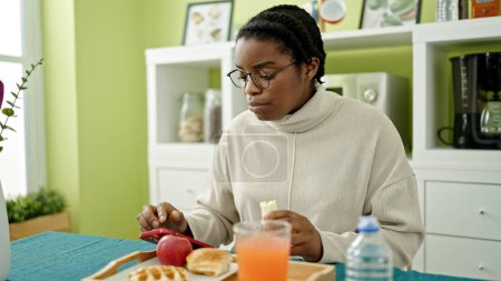 Téléchargez les photos : Femme afro-américaine prenant le petit déjeuner en utilisant un smartphone à la salle à manger - en image libre de droit