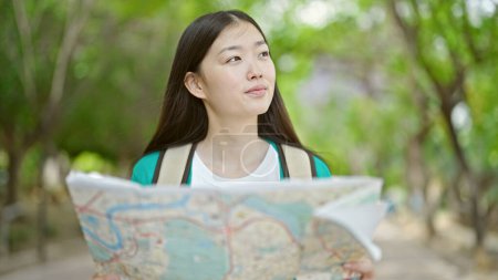 Téléchargez les photos : Jeune femme chinoise touriste portant un sac à dos regardant la carte de la ville au parc - en image libre de droit