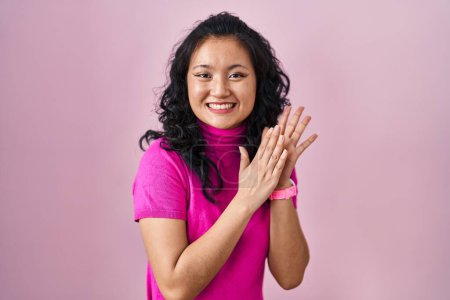 Foto de Joven asiática mujer de pie sobre rosa fondo aplaudiendo y aplaudiendo feliz y alegre, sonriendo orgullosas manos juntas - Imagen libre de derechos
