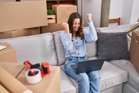 Photo for Young woman using laptop sitting on sofa at new home - Royalty Free Image